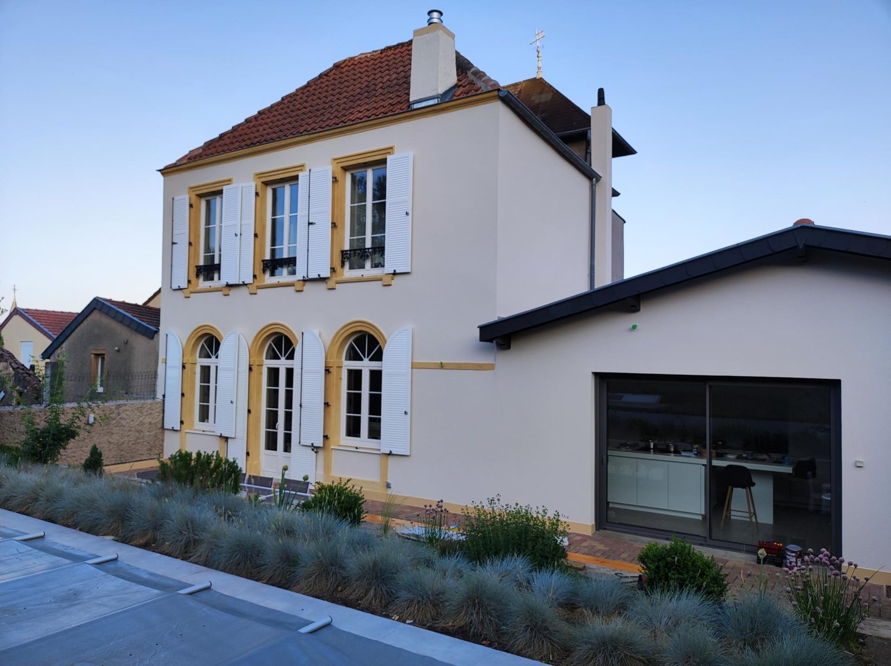 Maison de village aux encadrements ocre, façade blanche et volets